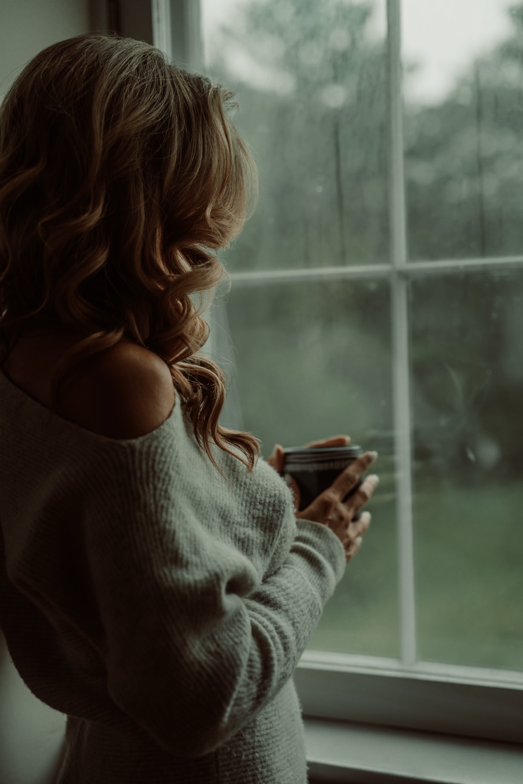 Client in a soft sweater holding coffee beside a studio window