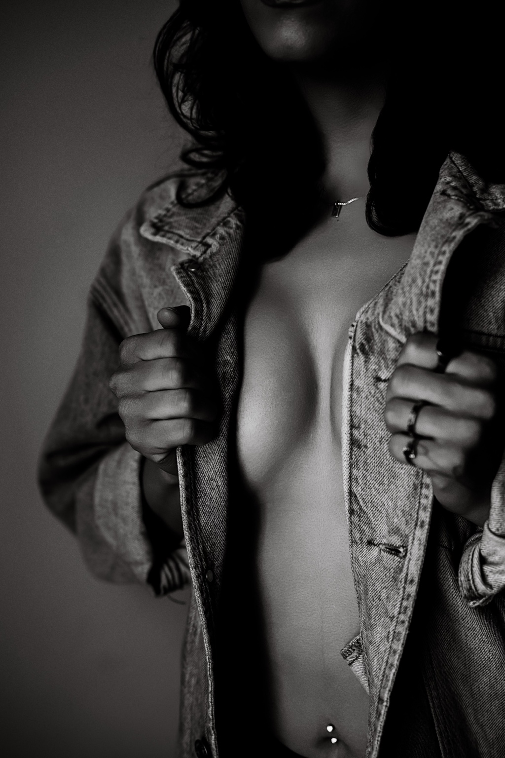 Black-and-white boudoir detail of a client holding open a denim jacket